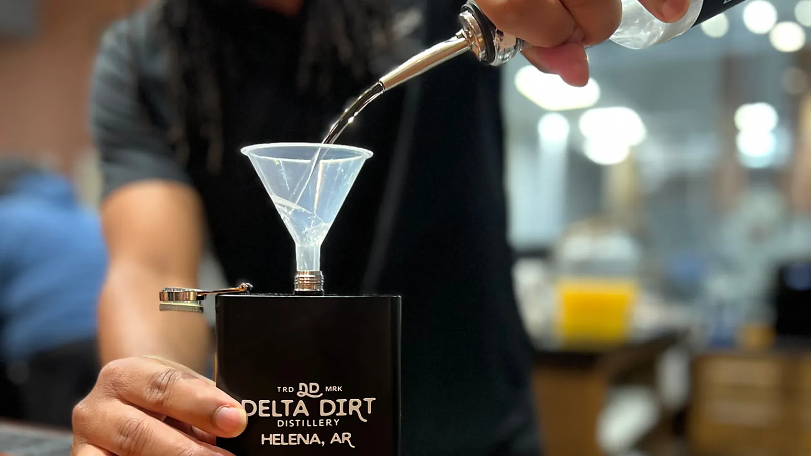A bartender at Delta Dirt Distillery in Helena pours a cocktail into a branded black flask.